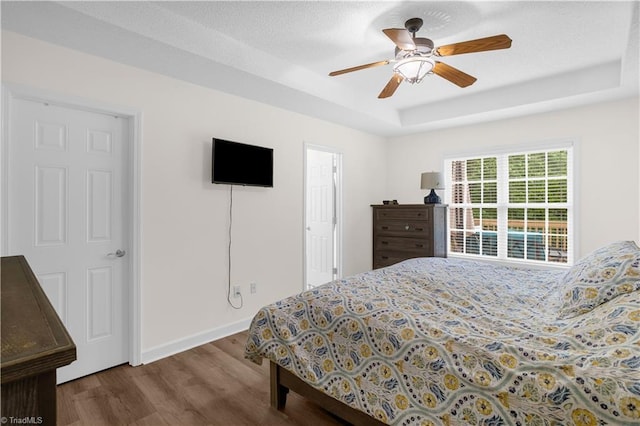 bedroom featuring baseboards, a tray ceiling, ceiling fan, and wood finished floors