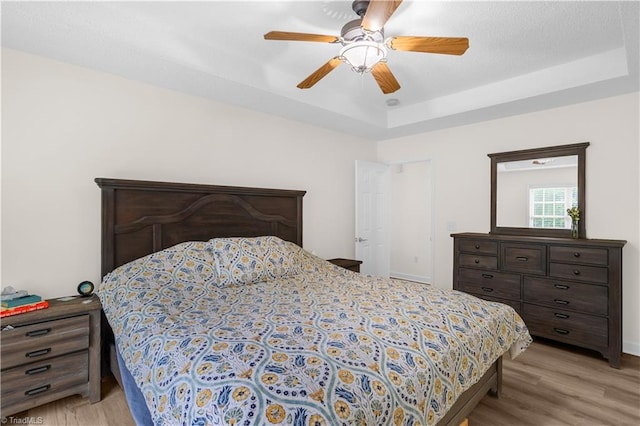 bedroom with a tray ceiling, ceiling fan, and light wood finished floors