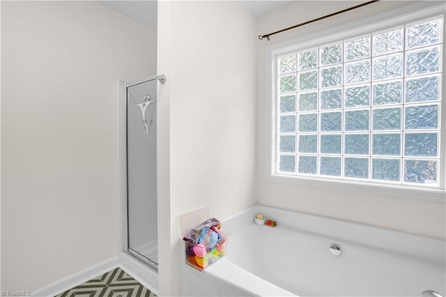 full bathroom with baseboards, a bath, a healthy amount of sunlight, and a shower stall