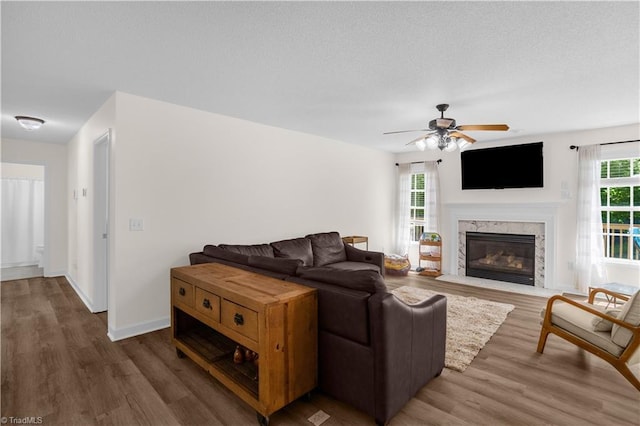 living area featuring a textured ceiling, ceiling fan, wood finished floors, and a fireplace