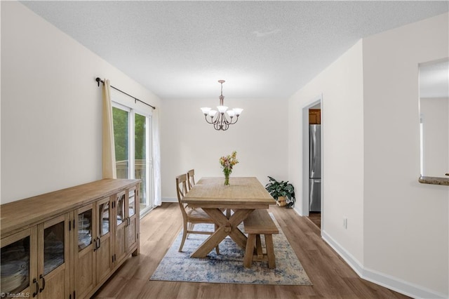dining room with baseboards, a textured ceiling, a notable chandelier, and wood finished floors