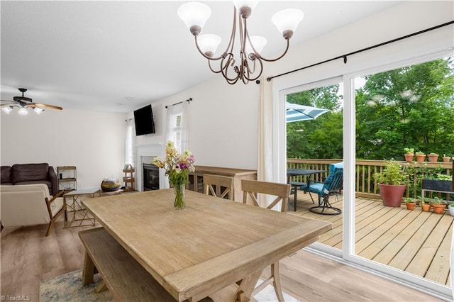 dining room with a glass covered fireplace, ceiling fan with notable chandelier, and wood finished floors