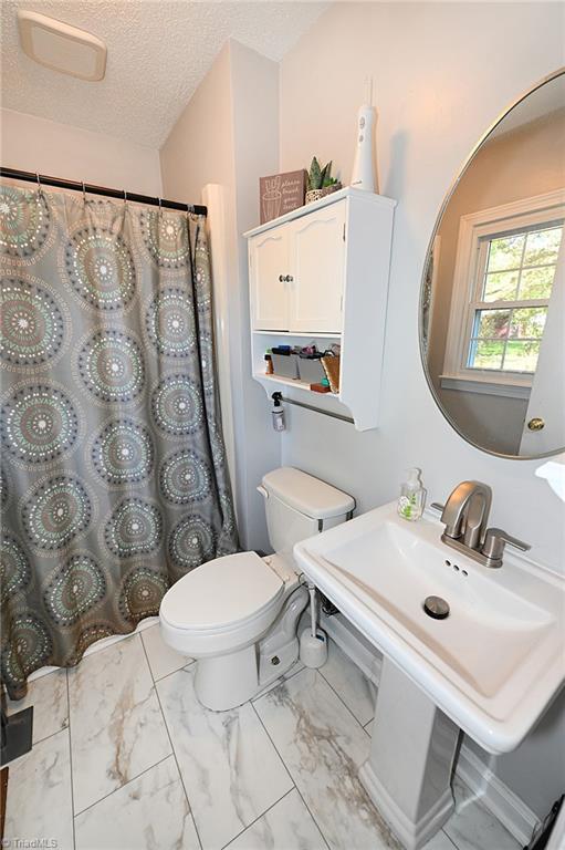 bathroom featuring toilet, a textured ceiling, sink, and curtained shower