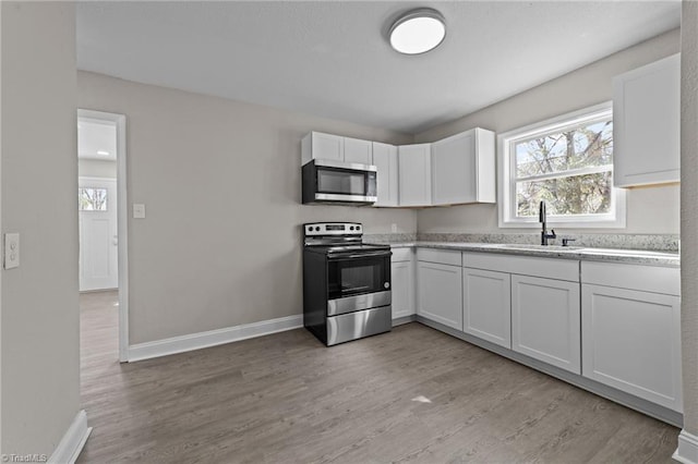 kitchen featuring baseboards, appliances with stainless steel finishes, light countertops, light wood-type flooring, and a sink