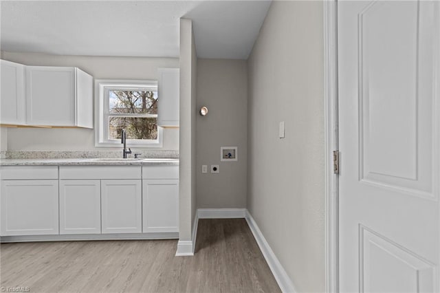 kitchen featuring baseboards, white cabinetry, a sink, and light wood finished floors