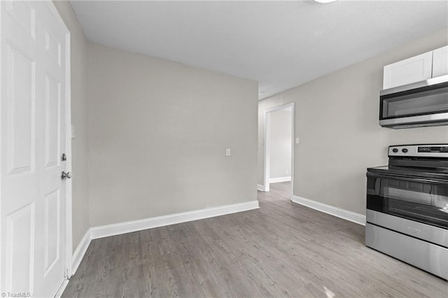 kitchen with white cabinets, appliances with stainless steel finishes, light wood-style flooring, and baseboards