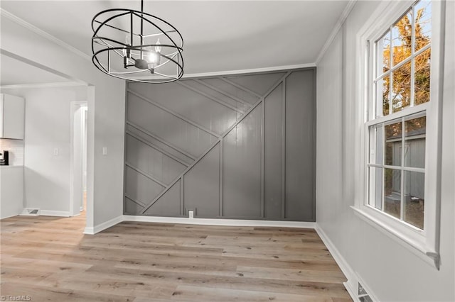 unfurnished dining area with ornamental molding, a notable chandelier, and light wood-type flooring