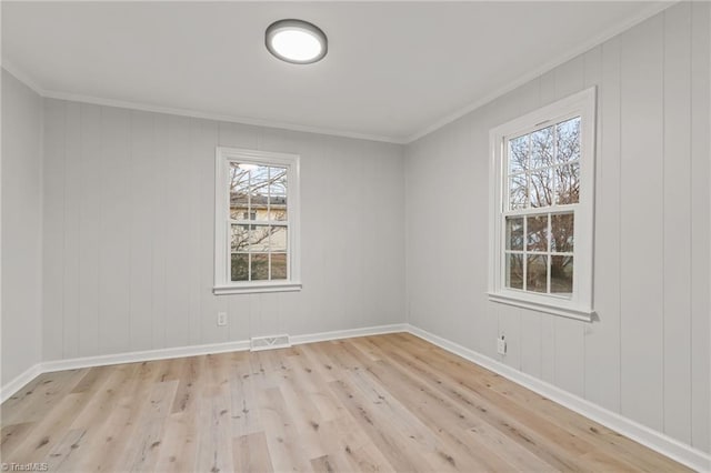 empty room with light hardwood / wood-style floors, a wealth of natural light, and crown molding