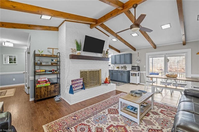 living room featuring ceiling fan, vaulted ceiling with beams, a fireplace, and light hardwood / wood-style flooring