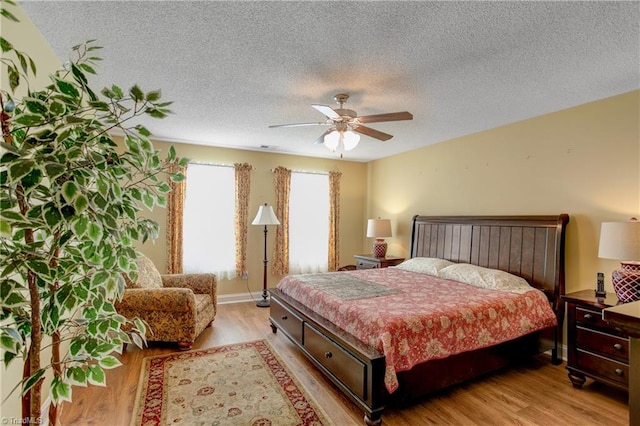 bedroom with ceiling fan, a textured ceiling, and light hardwood / wood-style flooring