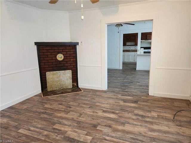 unfurnished living room featuring a brick fireplace, ornamental molding, dark wood-type flooring, and ceiling fan