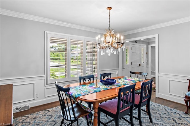 dining space featuring crown molding, a chandelier, a decorative wall, wood finished floors, and wainscoting