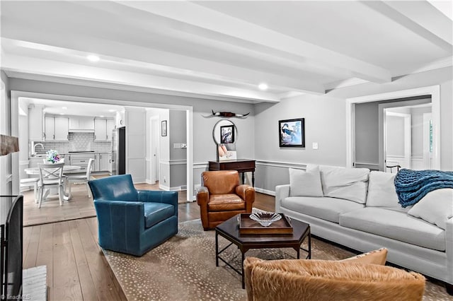living area featuring light wood-style flooring, beam ceiling, recessed lighting, and wainscoting