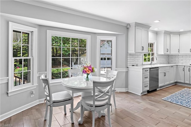 kitchen featuring stainless steel dishwasher, decorative backsplash, light wood-type flooring, healthy amount of natural light, and ornamental molding