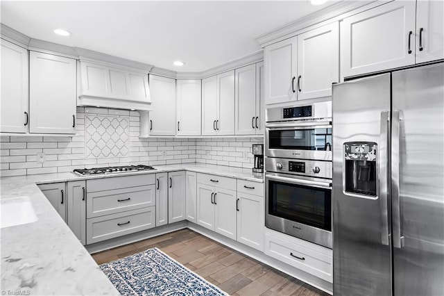 kitchen with stainless steel appliances, white cabinets, tasteful backsplash, wood finished floors, and recessed lighting
