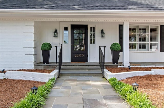 entrance to property featuring roof with shingles and a porch