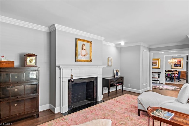 living area featuring wood finished floors, a chandelier, baseboards, crown molding, and a fireplace