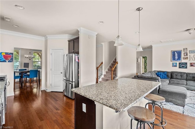 kitchen with stainless steel refrigerator with ice dispenser, a breakfast bar, dark brown cabinetry, crown molding, and hanging light fixtures