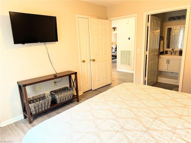 bedroom featuring baseboards, visible vents, wood finished floors, ensuite bathroom, and a sink