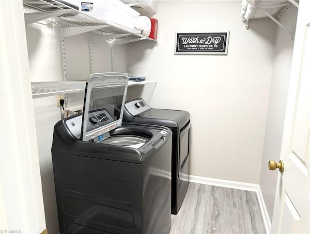 clothes washing area with laundry area, light wood-type flooring, independent washer and dryer, and baseboards