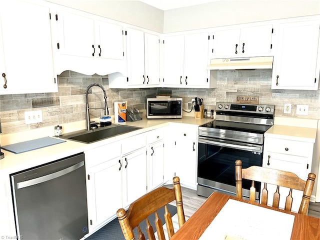 kitchen with stainless steel appliances, tasteful backsplash, light countertops, a sink, and under cabinet range hood