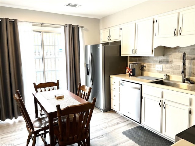 kitchen with visible vents, backsplash, white cabinets, a sink, and dishwashing machine