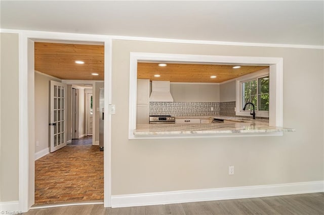 kitchen with backsplash, premium range hood, wood-type flooring, sink, and white cabinets