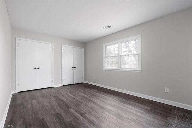 unfurnished bedroom featuring dark hardwood / wood-style floors and multiple closets