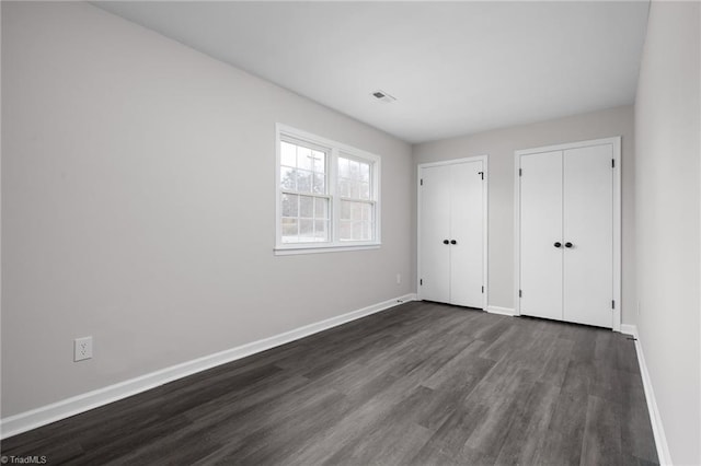 unfurnished bedroom with two closets and dark wood-type flooring