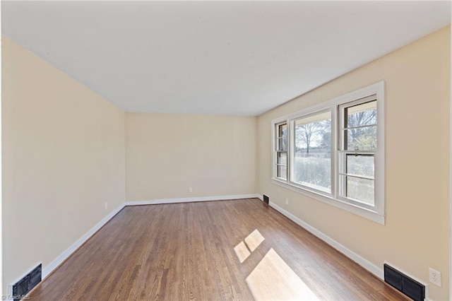 empty room featuring visible vents, baseboards, and wood finished floors