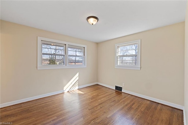 unfurnished room with baseboards, visible vents, and wood finished floors