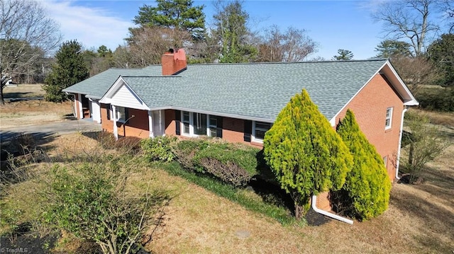 exterior space featuring brick siding, driveway, a chimney, and roof with shingles