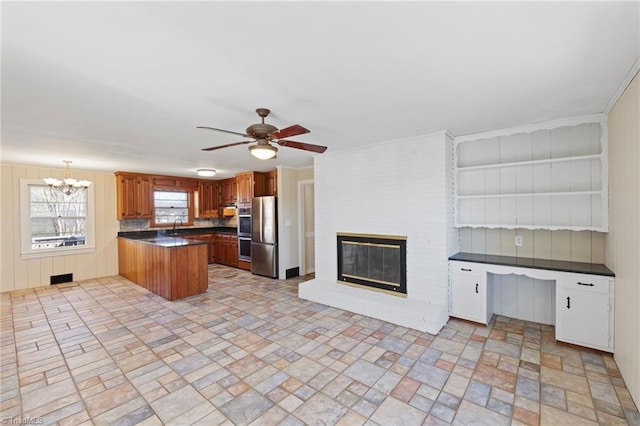 kitchen featuring dark countertops, a peninsula, a fireplace, a sink, and ceiling fan with notable chandelier