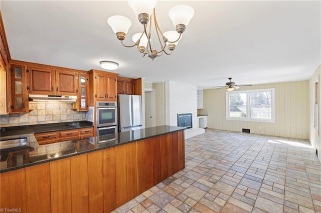 kitchen featuring brown cabinets, a fireplace, stainless steel appliances, a peninsula, and under cabinet range hood