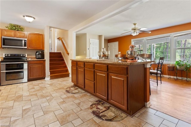kitchen with brown cabinets, stainless steel appliances, a kitchen island, baseboards, and ceiling fan