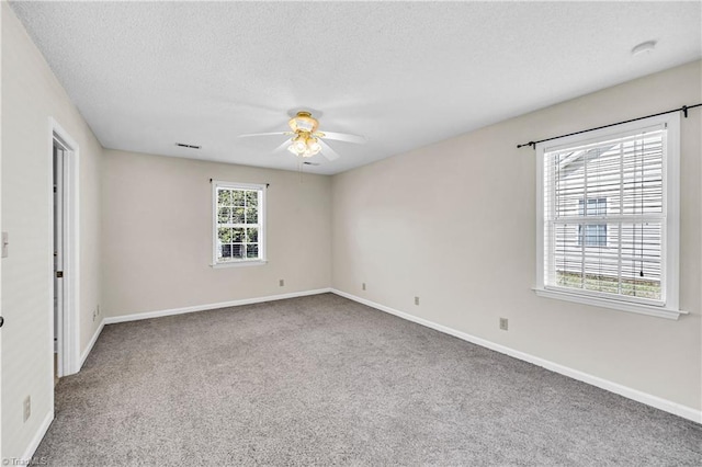 carpeted spare room featuring visible vents, a ceiling fan, baseboards, and a textured ceiling