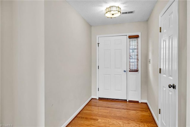 doorway to outside featuring visible vents, a textured ceiling, light wood-type flooring, and baseboards