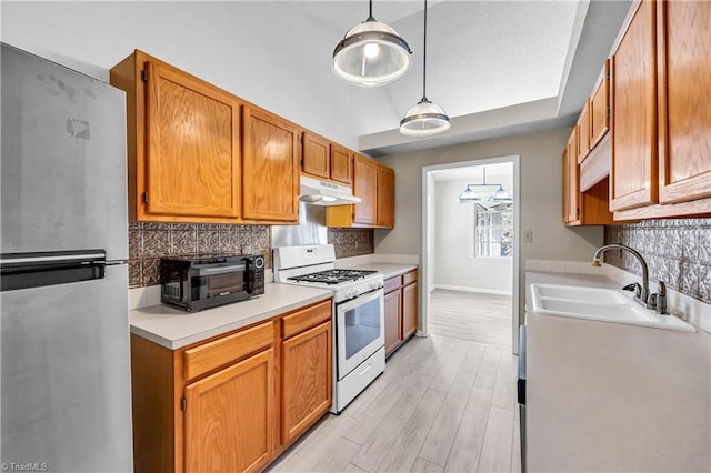 kitchen featuring gas range gas stove, freestanding refrigerator, a sink, light countertops, and under cabinet range hood