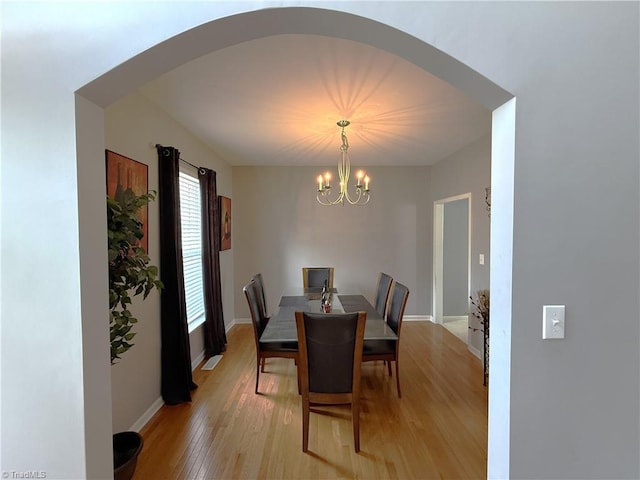 dining area featuring arched walkways, light wood-style flooring, baseboards, and an inviting chandelier