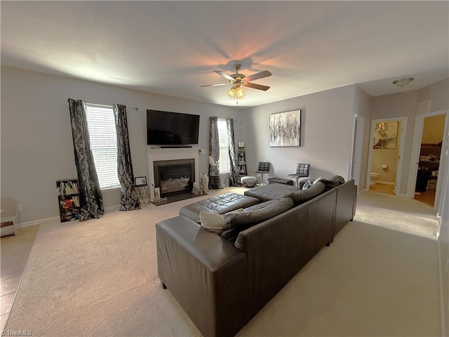 living area featuring a fireplace with flush hearth, light carpet, ceiling fan, and baseboards