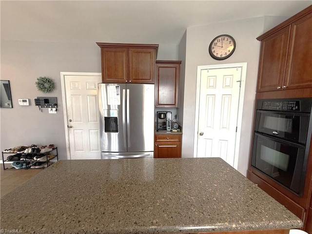 kitchen featuring dark stone countertops, stainless steel fridge, and dobule oven black