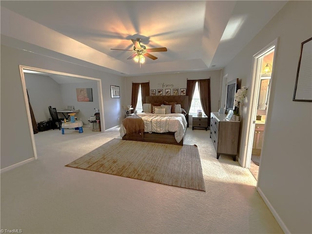 bedroom featuring light carpet, a tray ceiling, connected bathroom, and baseboards