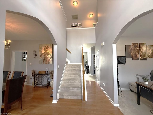 foyer entrance with baseboards, visible vents, arched walkways, stairway, and wood finished floors