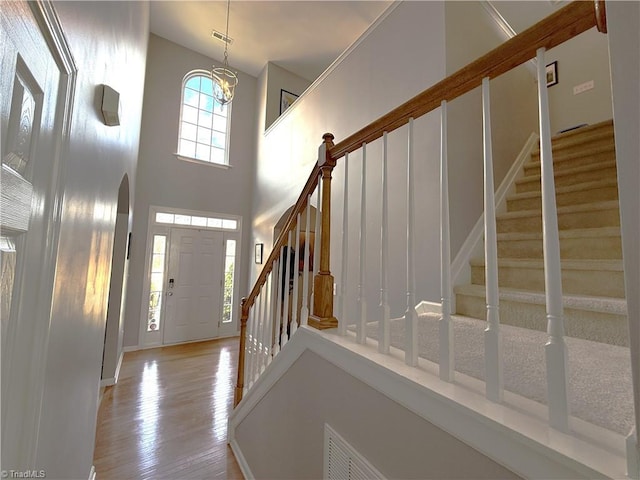 entrance foyer with arched walkways, wood finished floors, stairs, a high ceiling, and a notable chandelier