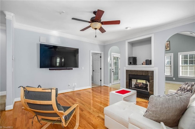 living room featuring wood-type flooring, plenty of natural light, ornamental molding, and a high end fireplace