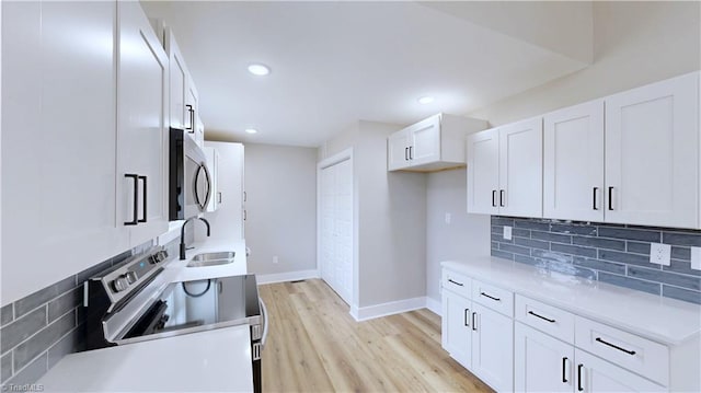 kitchen with sink, appliances with stainless steel finishes, light hardwood / wood-style floors, white cabinets, and decorative backsplash