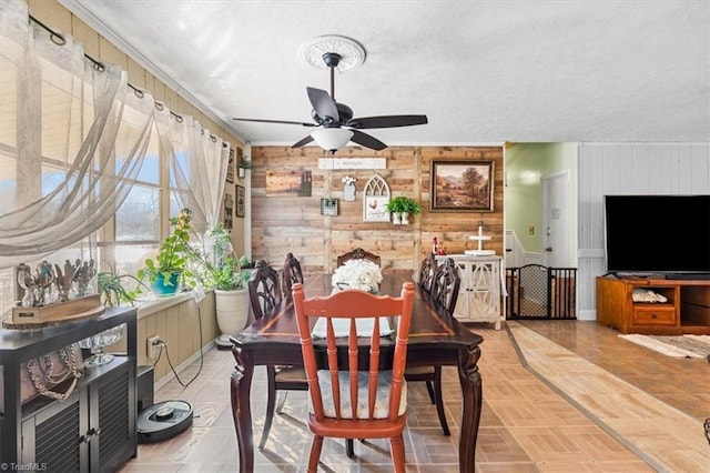 dining space featuring wooden walls, ceiling fan, a textured ceiling, and parquet flooring