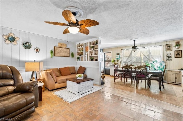 living room featuring wood walls, ceiling fan, and a textured ceiling