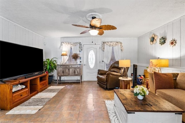 living room featuring ceiling fan, a textured ceiling, and wooden walls