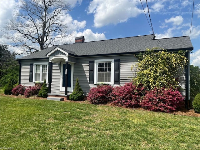 view of front of home with a front yard, a shingled roof, and a chimney